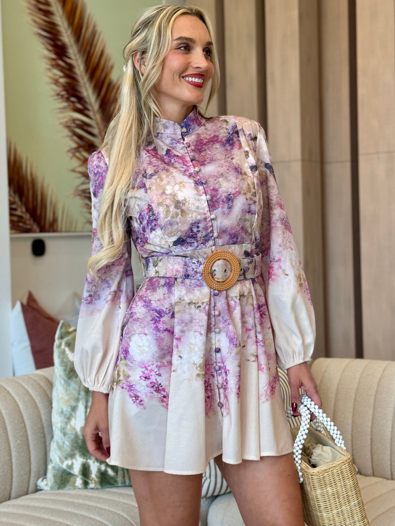 Woman in watercolor floral mini dress with belted waist and long sleeves.