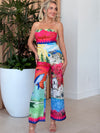 Woman in strapless scenic print jumpsuit with whales, coastlines, and florals.