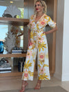 Woman in belted tropical floral jumpsuit with soft yellow and blush print.