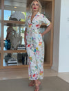 Woman in white floral jumpsuit with short sleeves and collared neckline.